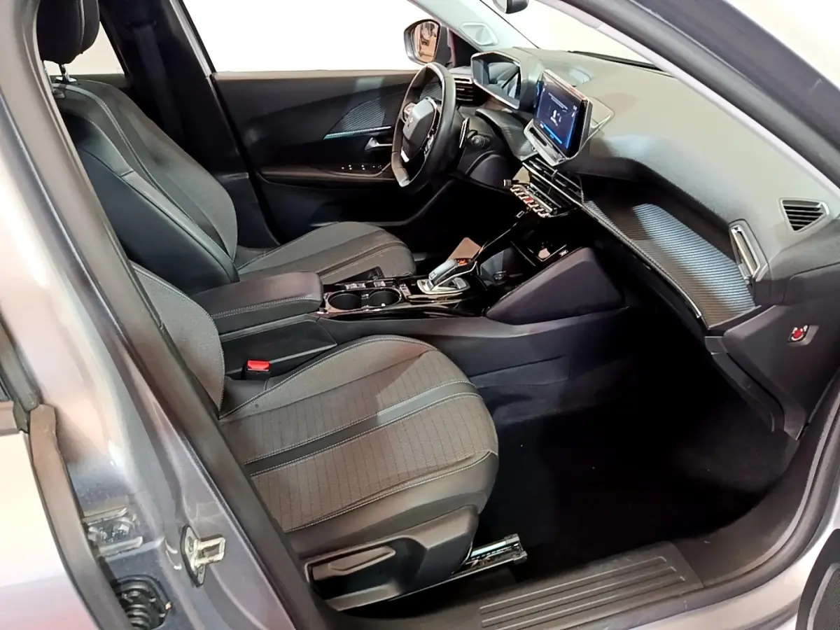 Vue intérieure côté conducteur du Peugeot 2008 gris clair, mettant en valeur les sièges, le volant cuir et l'écran tactile central.