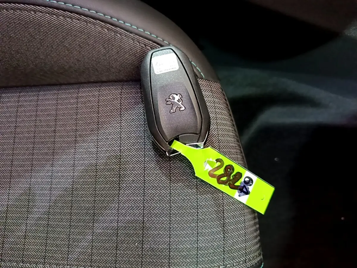 Gros plan sur la clé Peugeot posée sur un siège en tissu gris foncé à motifs, intérieur du Peugeot 2008 2021.