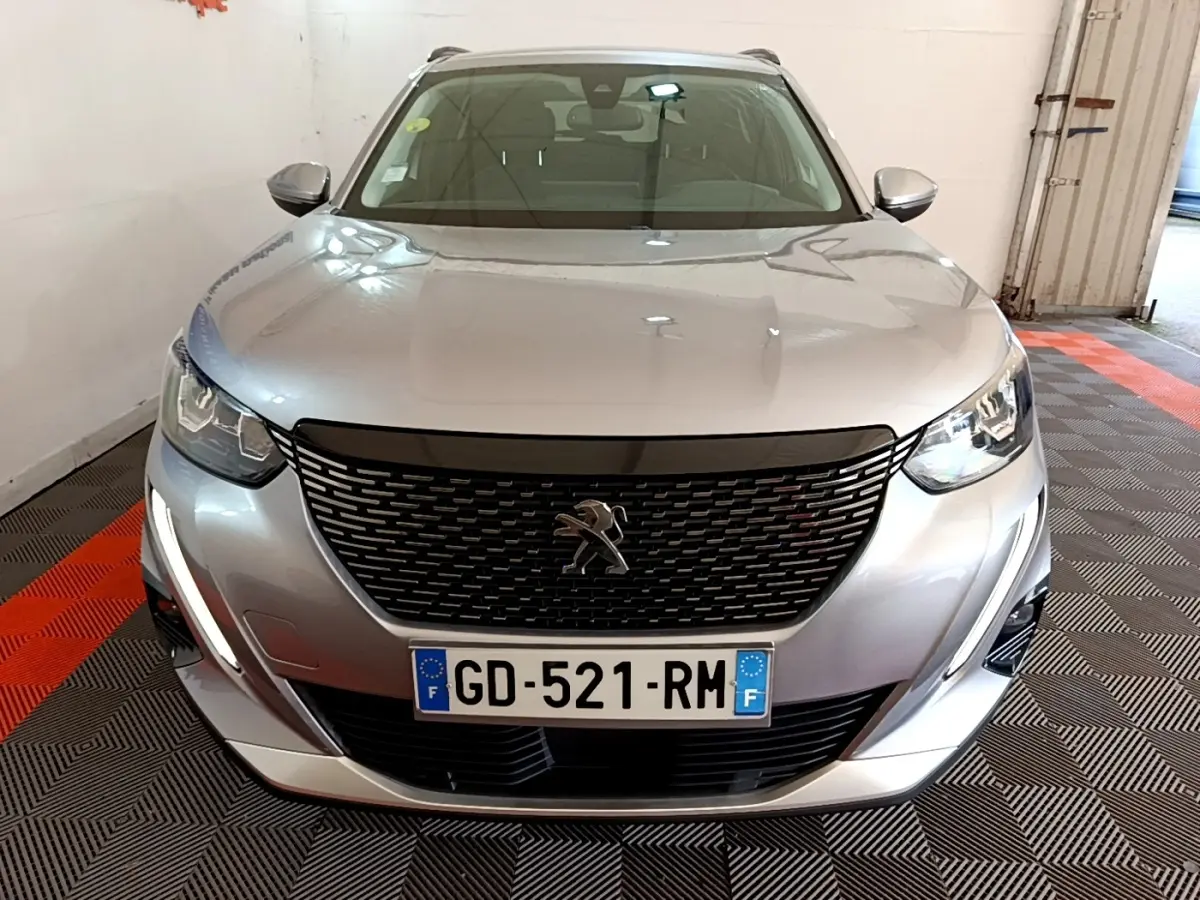 Vue avant d'un Peugeot 2008 gris clair 2021 avec calandre noire et feux LED allumés en intérieur.