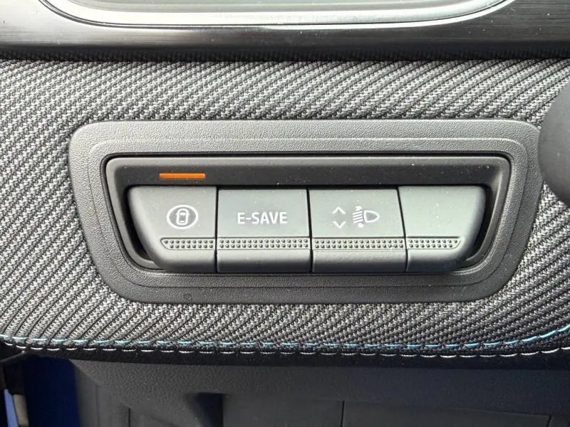Gros plan sur les boutons de commande du tableau de bord avec finition carbone et surpiqûres bleues du Renault Captur hybride 2026.