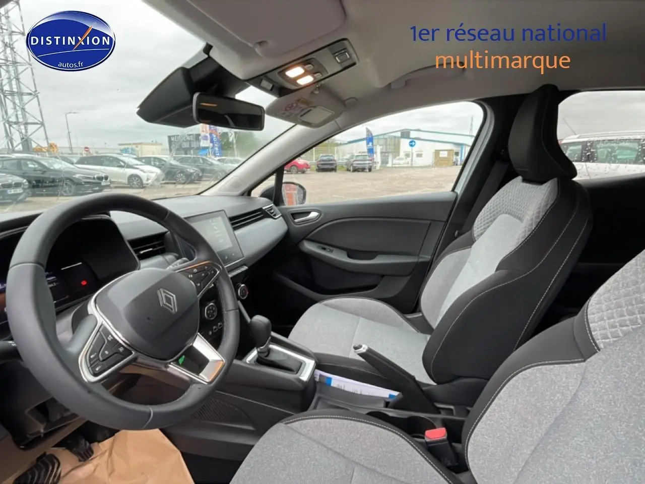 Vue intérieure côté conducteur de la Renault Clio V 2025 avec sièges gris à motif 3D et volant multifonction.