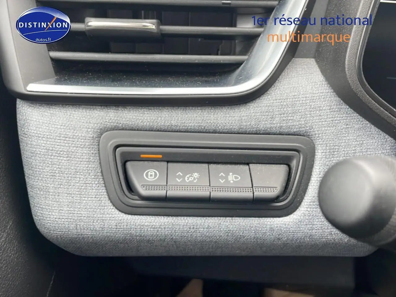 Gros plan sur les commandes d'éclairage et verrouillage, tissu gris à motif 3D dans une Renault Clio V blanche.