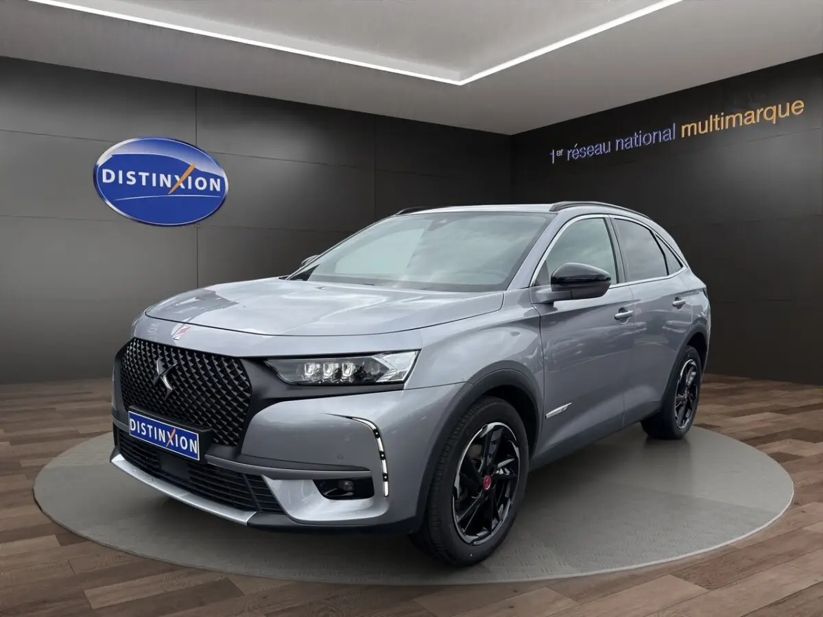 Vue 3/4 avant droit d'un DS7 Crossback gris clair avec calandre noire et jantes noires brillantes dans un showroom.