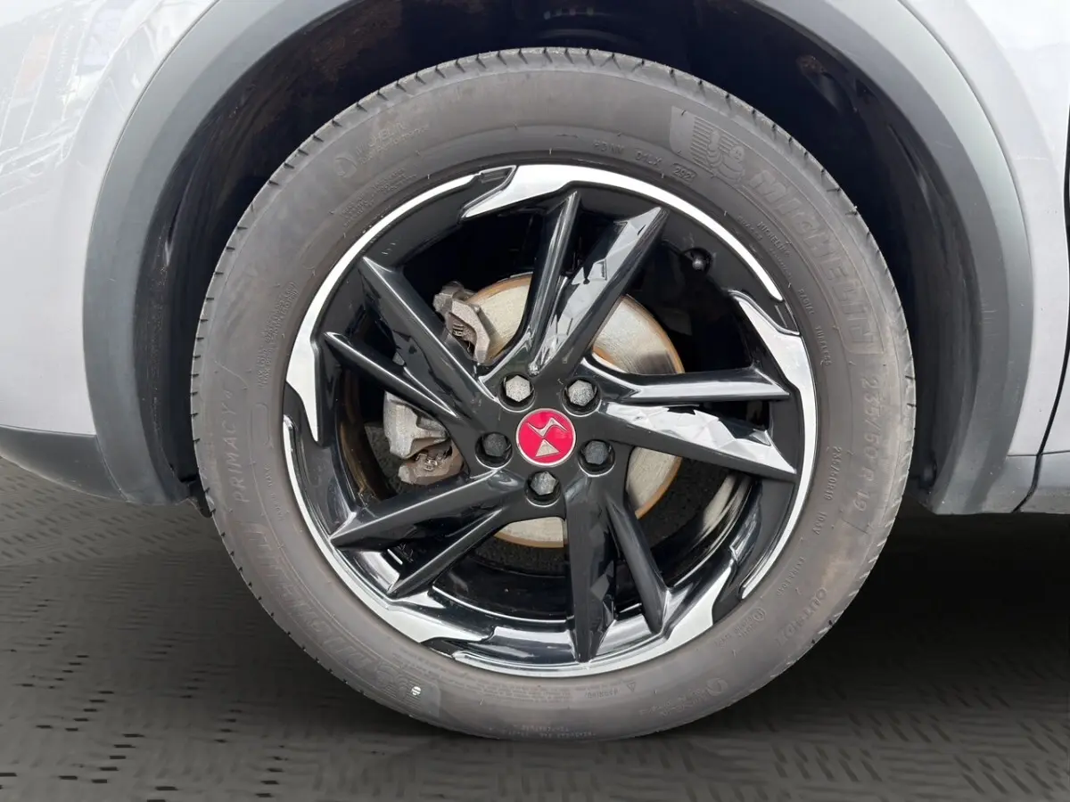 Gros plan sur la roue avant droite du DS7 Crossback gris clair, jante noire brillante avec logo rouge au centre.