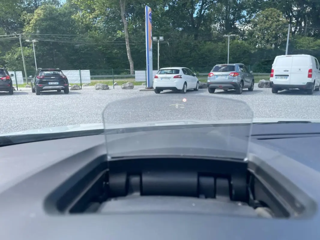 Affichage tête haute visible depuis l'intérieur d'une Renault Mégane IV blanche, vue avant sur un parking extérieur.