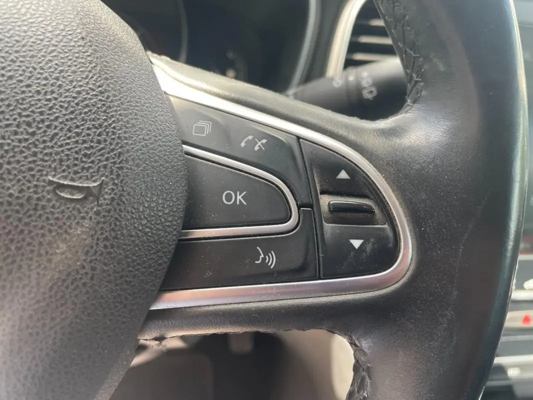 Gros plan sur les commandes multifonctions à droite du volant noir de la Renault Mégane IV blanche de 2016.