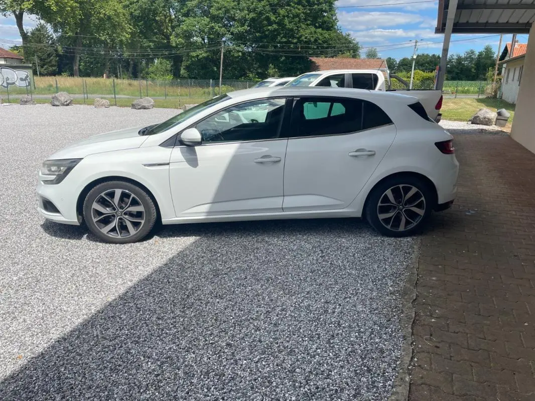 Renault Mégane IV blanche vue de profil côté gauche, garée sur gravier avec jantes alliage noires et grises.