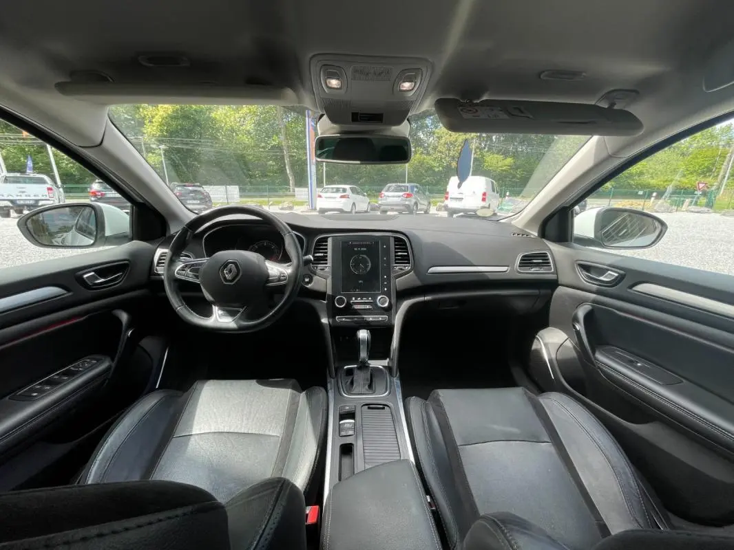 Vue intérieure avant de la Renault Mégane IV blanche de 2016, montrant le tableau de bord et les sièges en cuir noir.