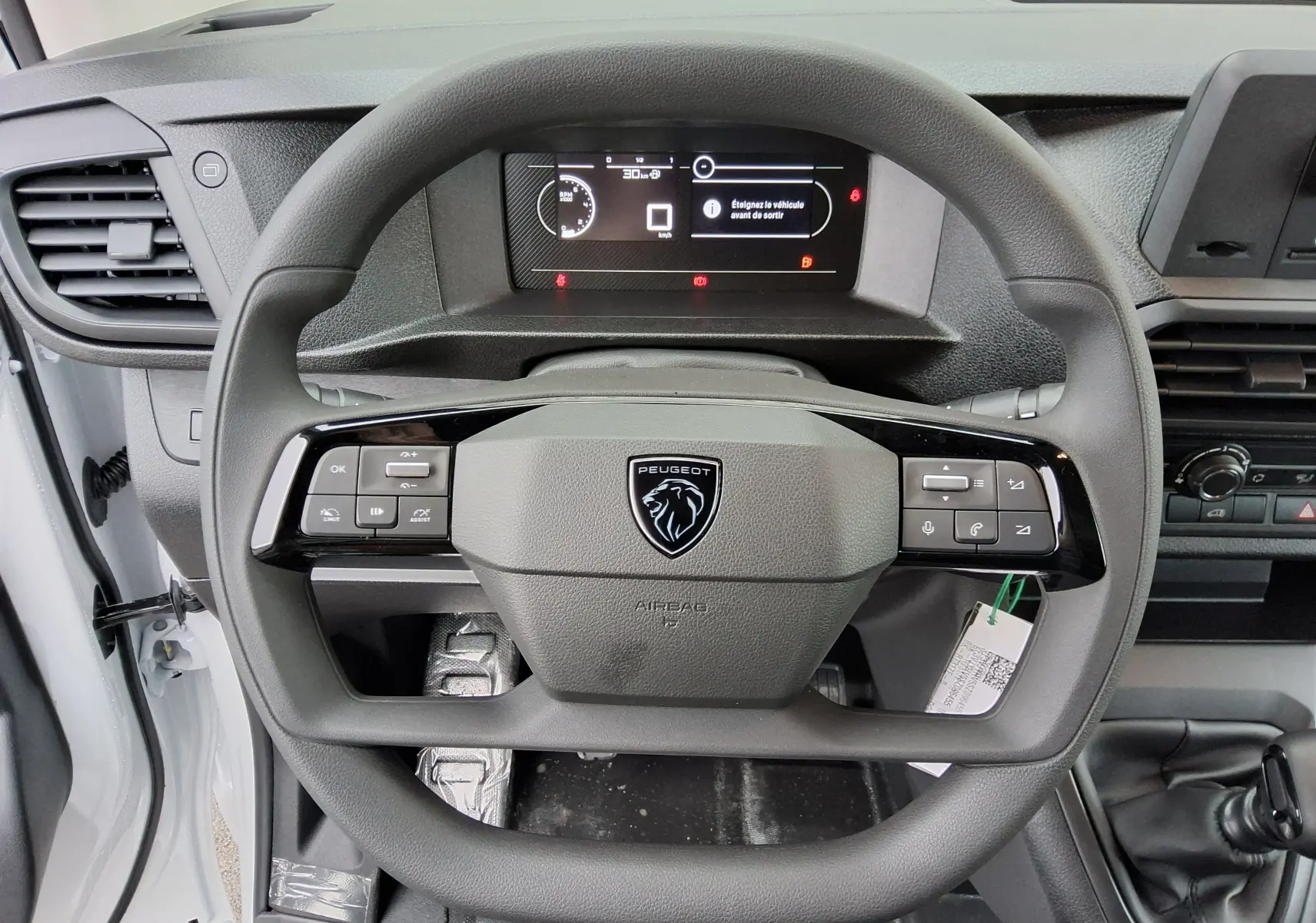 Vue rapprochée du volant noir du Peugeot Expert Fourgon blanc 2025 avec tableau de bord numérique et commande au volant.