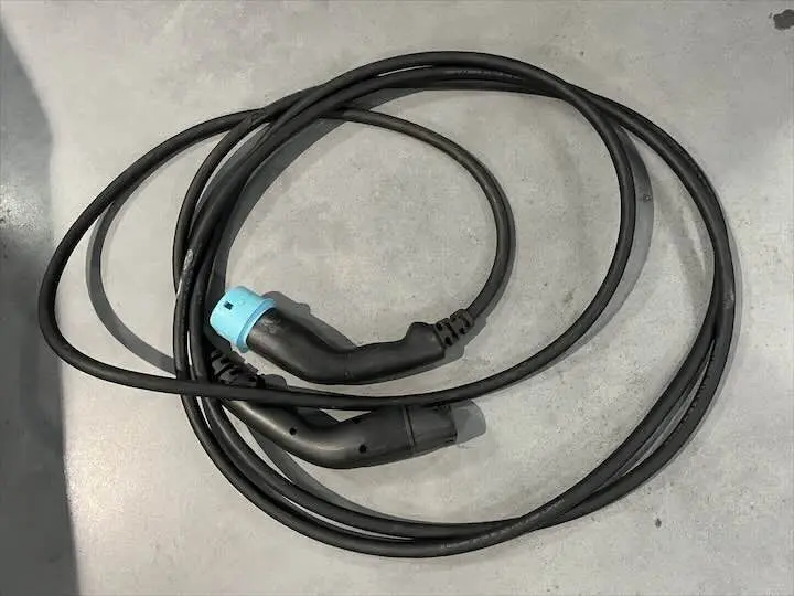 Câble de recharge noir pour Renault ZOE blanc Glacier, posé enroulé sur sol gris.