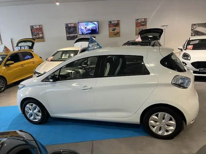 Profil côté gauche d'une Renault ZOE blanche glacier R90 LIFE 41 kWh 2019 en showroom avec d'autres véhicules visibles.
