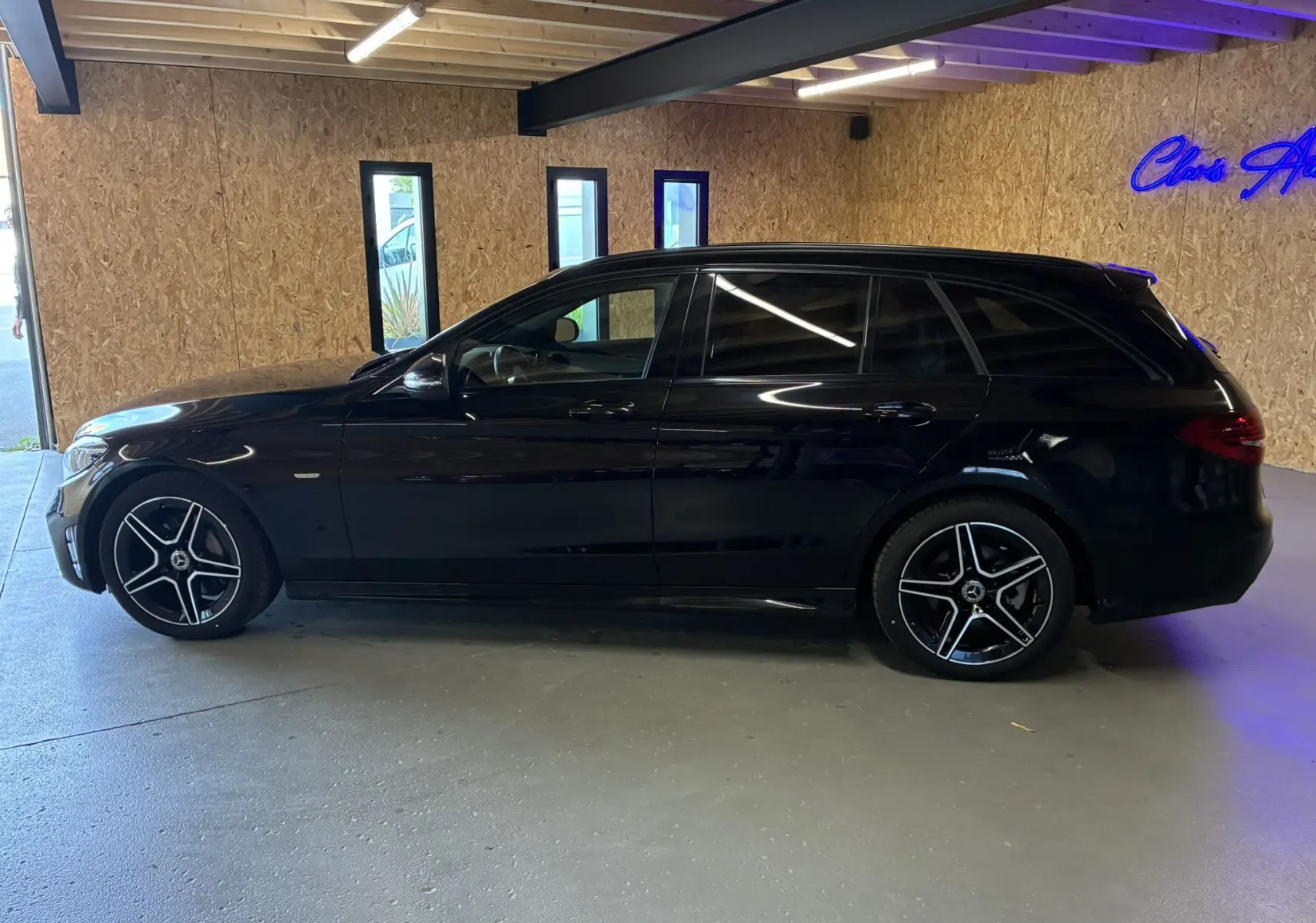 Profil droit d'un break Mercedes Classe C 220D AMG Line noir métal avec jantes alu bi-ton dans un garage.