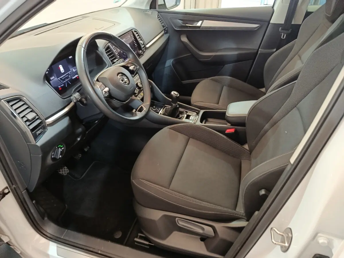 Intérieur avant droit d'un Skoda Karoq blanc 2024, sièges tissu noirs et tableau de bord avec écran tactile.