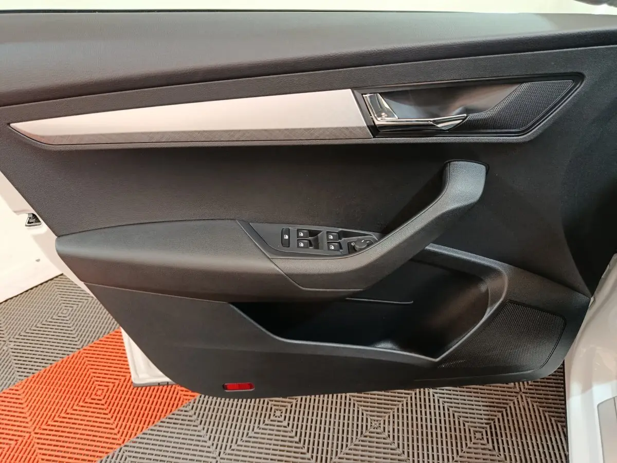 Vue rapprochée de la porte avant gauche noire du Skoda Karoq blanc, avec commandes de vitres et poignée chromée.