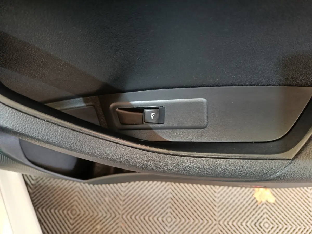 Détail de la commande d'ouverture de coffre sur la porte intérieure côté gauche d'un Skoda Karoq blanc 2024.