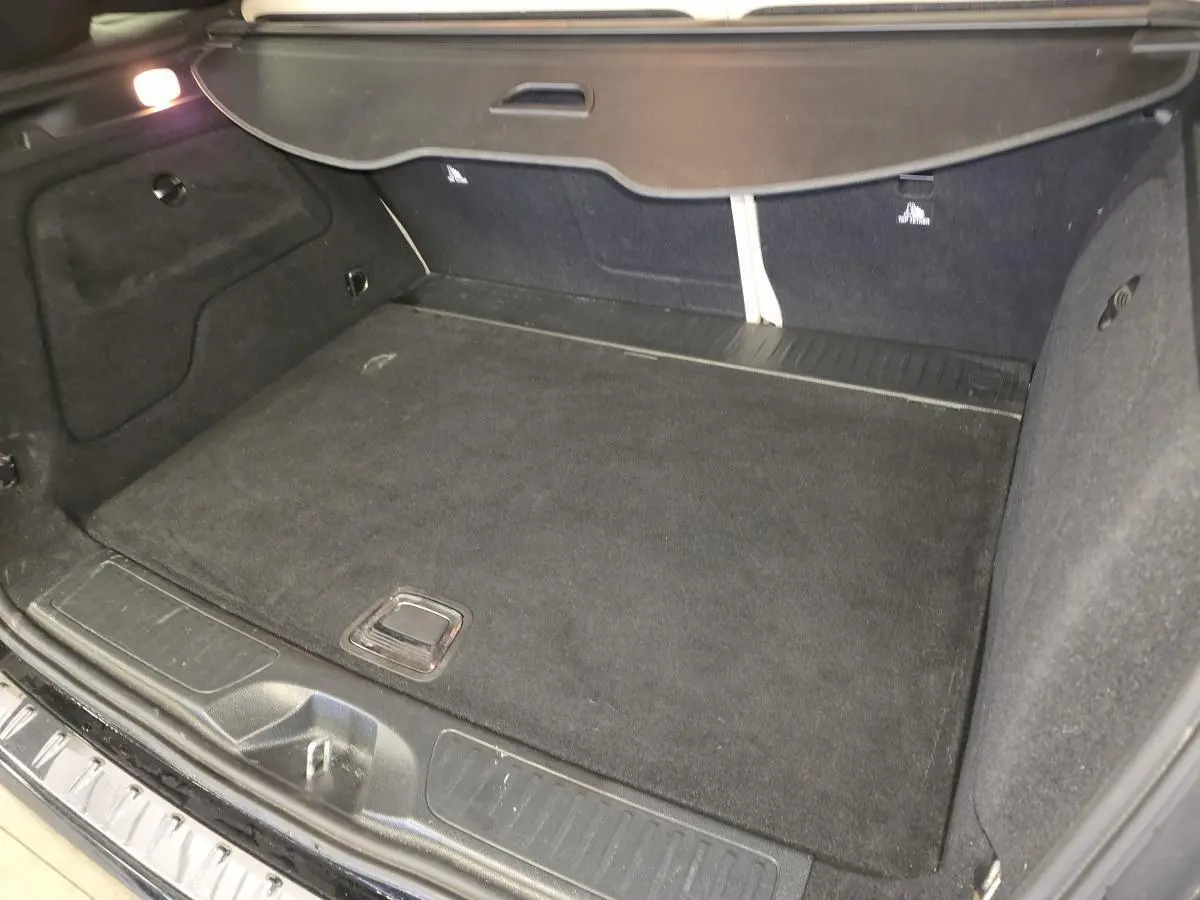 Coffre ouvert de la Mercedes Classe B 180 d Intuition noir, montrant un espace de chargement propre et tapis noir.