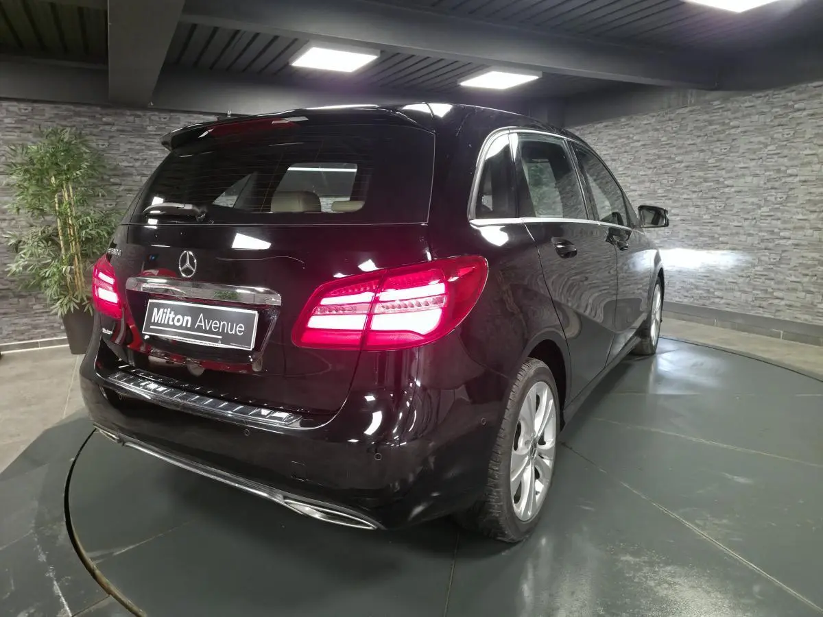 Vue 3/4 arrière droite d'une Mercedes Classe B noire avec feux arrière allumés dans un showroom.
