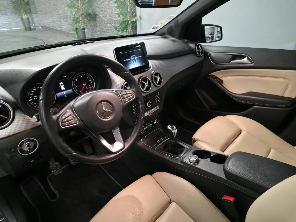 Intérieur de Mercedes Classe B 180 d 2018, vue côté conducteur, sièges beige et volant cuir noir avec commandes multifonctions.