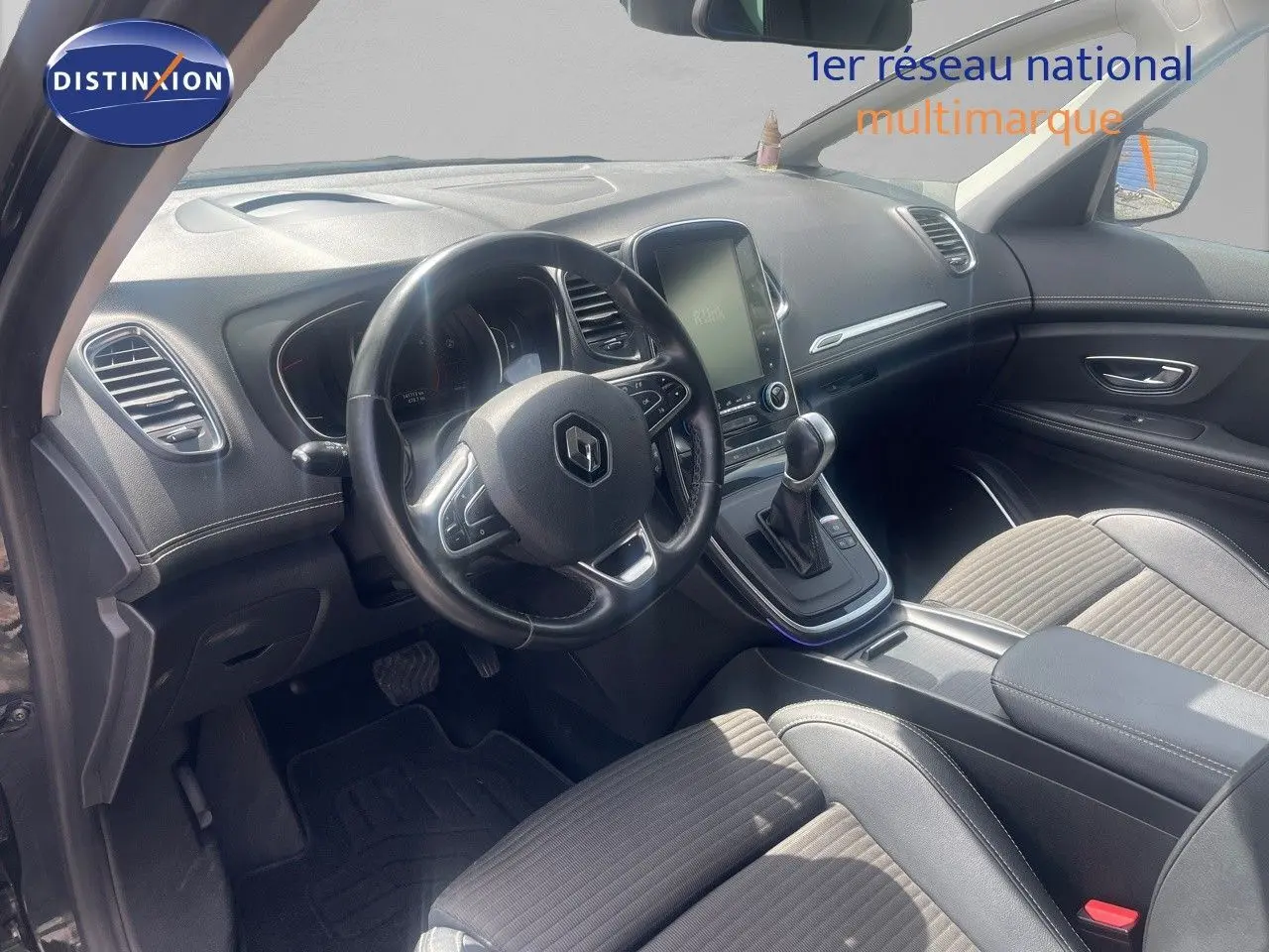 Vue intérieure côté conducteur du Renault Scénic IV noir, mettant en valeur le tableau de bord et la console centrale avec écran tactile.