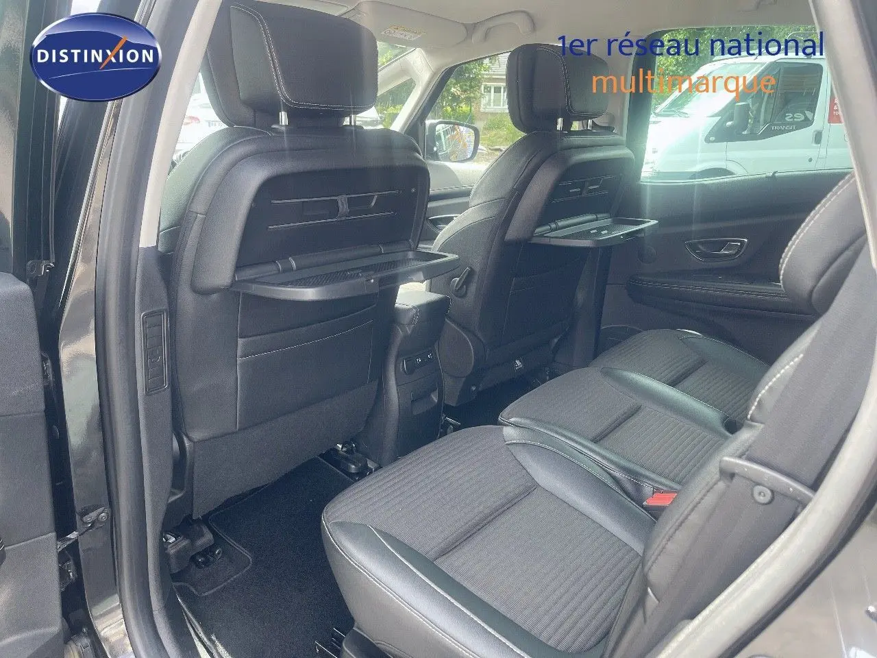 Vue intérieure arrière du Renault Scénic IV noir, montrant les sièges en tissu avec tablettes rabattables intégrées aux dossiers avant.