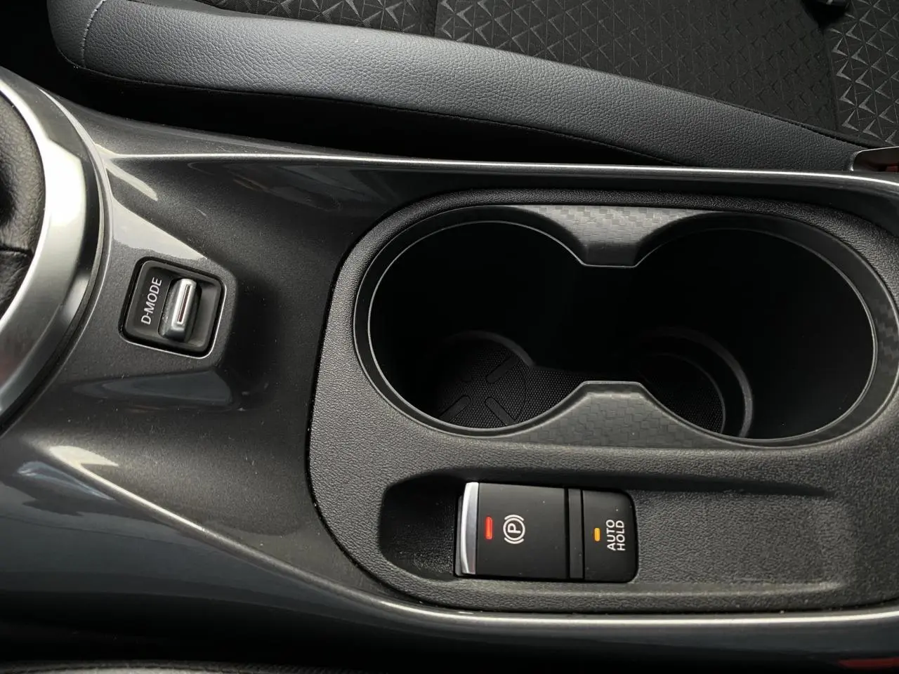 Gros plan sur la console centrale noire du Nissan Juke blanc perle, avec bouton frein électrique et porte-gobelets.