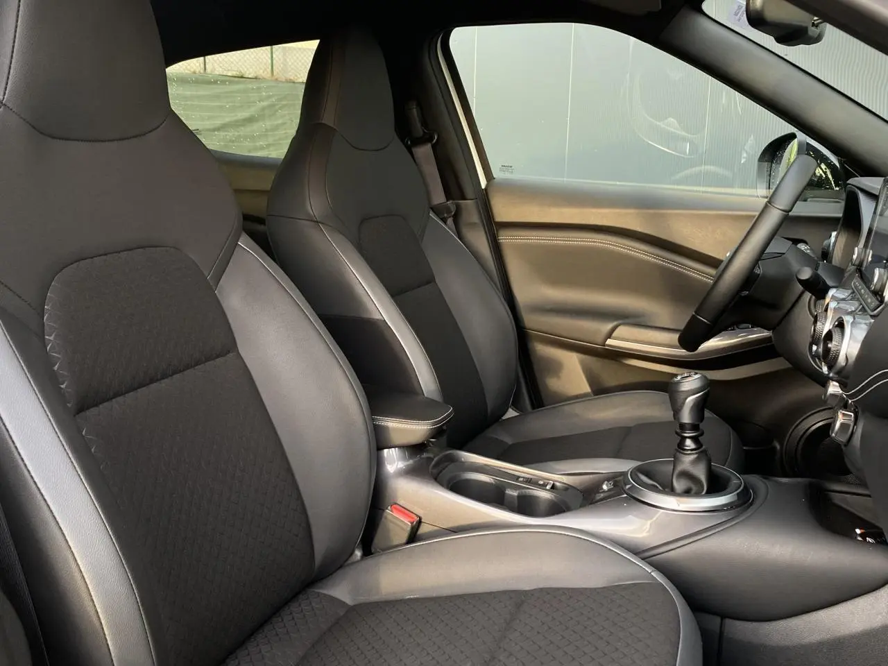 Intérieur du Nissan Juke N-Connecta 2024, vue côté conducteur, sellerie mixte noire avec volant et levier de vitesse manuels.