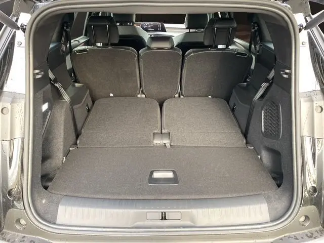 Vue arrière du coffre ouvert du Peugeot 5008 noir Perla Nera, montrant les sièges arrière partiellement rabattus et l'espace de chargement plat.