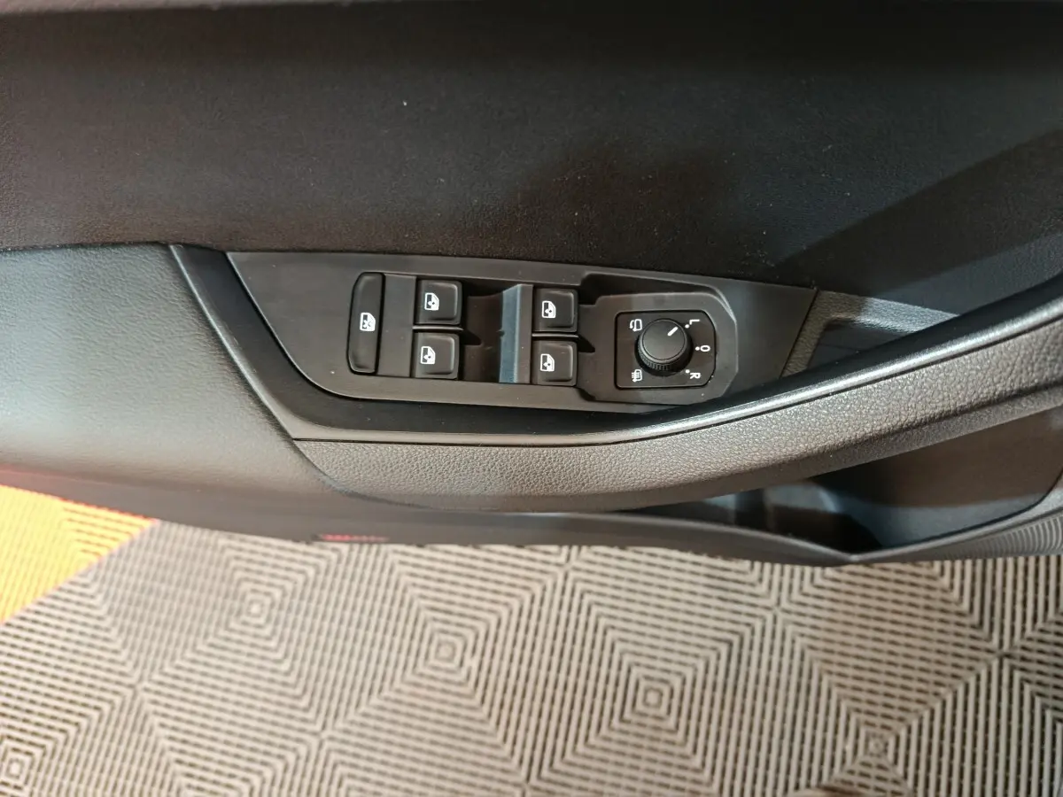 Gros plan sur les commandes des vitres et des rétroviseurs côté conducteur d’un Skoda Karoq blanc 2024.