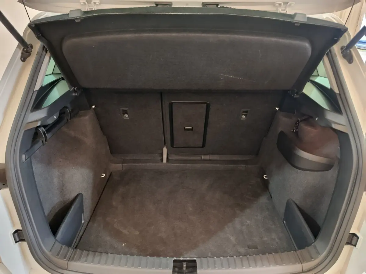 Coffre ouvert vu de l'arrière d'un Skoda Karoq blanc 2024, espace de chargement avec banquette rabattable et trappe à ski.