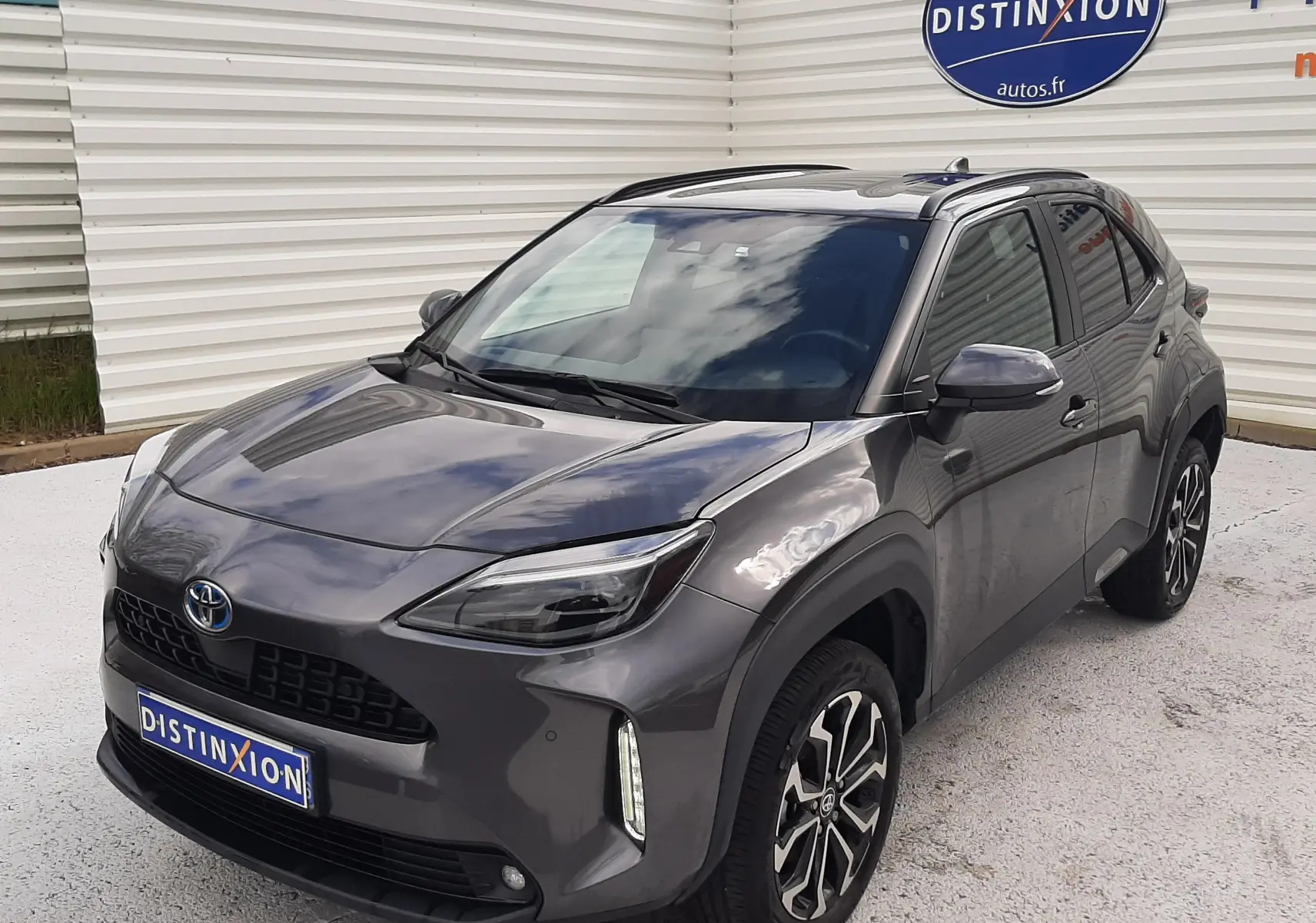 Toyota Yaris Cross gris atlas métal vue 3/4 avant droit, avec jantes alliage bicolores et toit noir brillant.