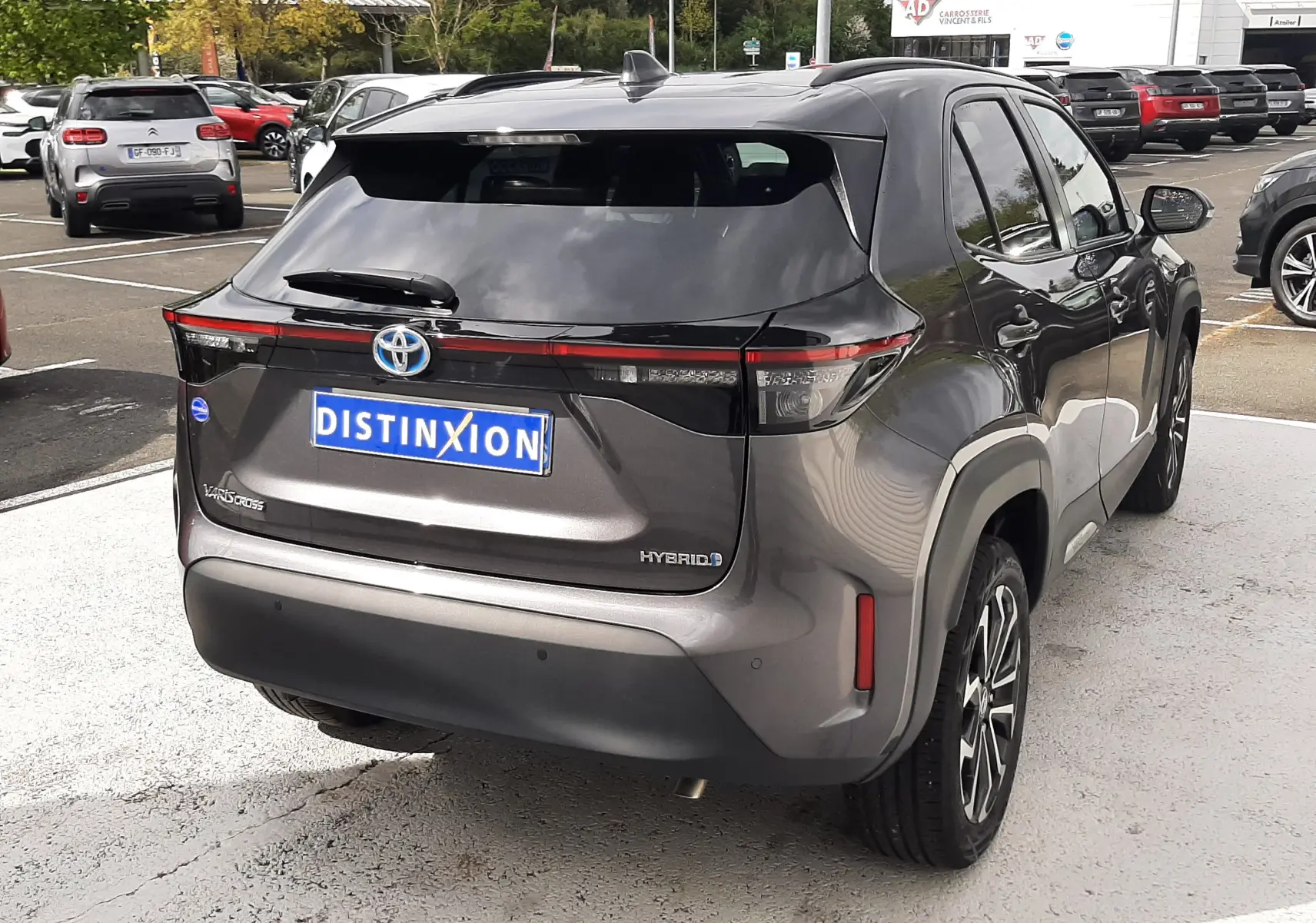 Vue 3/4 arrière droite d'une Toyota Yaris Cross 2024 gris atlas métal avec logo hybride et feux arrière fins à LED.