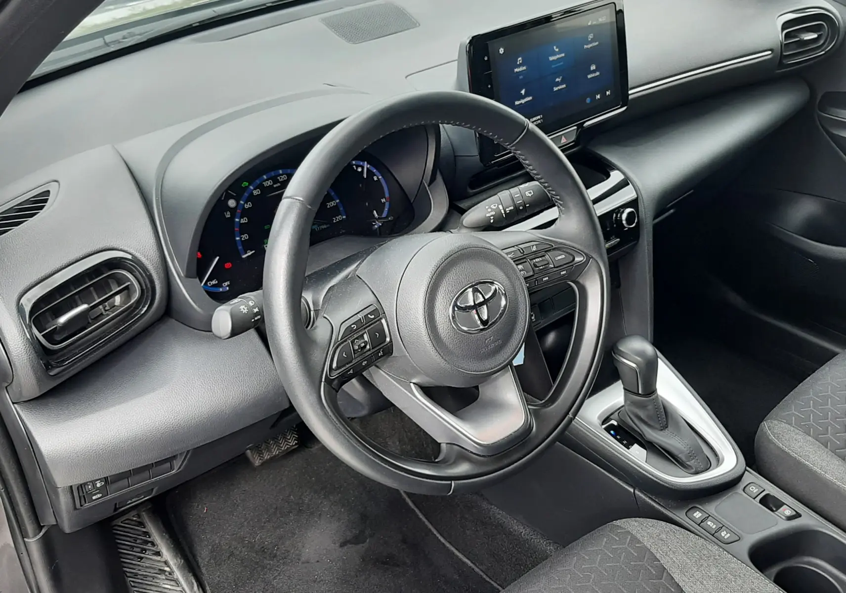 Vue intérieure côté conducteur de la Toyota Yaris Cross 2024, tableau de bord gris avec écran tactile et volant multifonction.