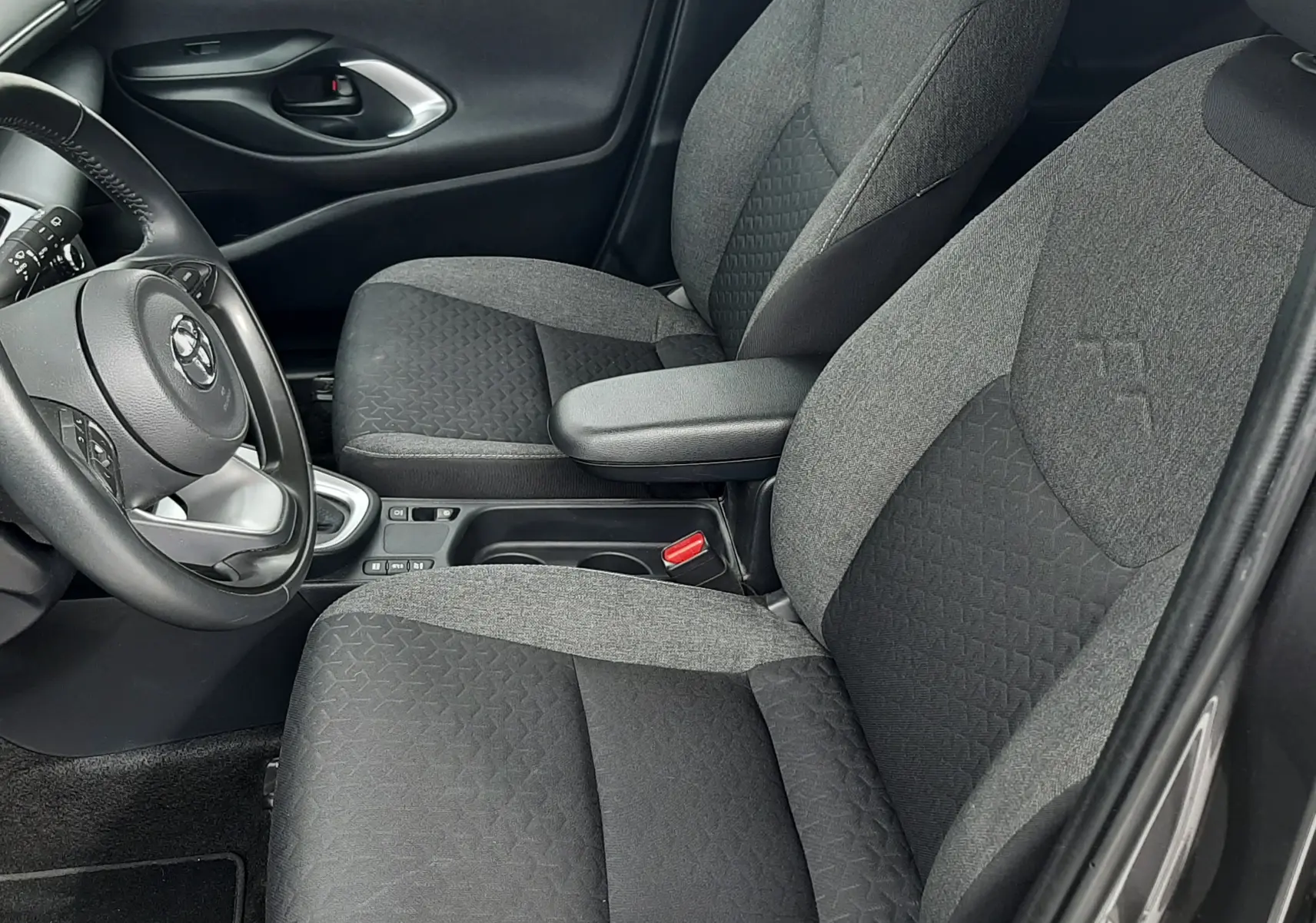Vue intérieure côté conducteur de la Toyota Yaris Cross 2024, sièges tissu gris bicolore avec accoudoir central.