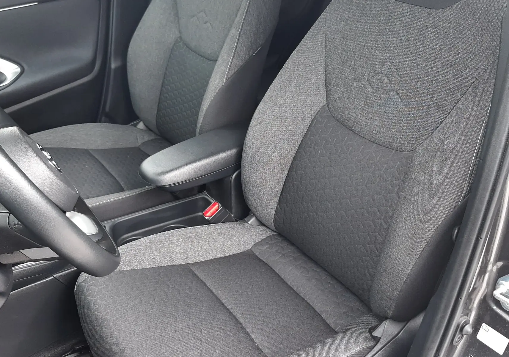 Vue intérieure rapprochée des sièges avant en tissu gris foncé et clair de la Toyota Yaris Cross 2024 hybride.