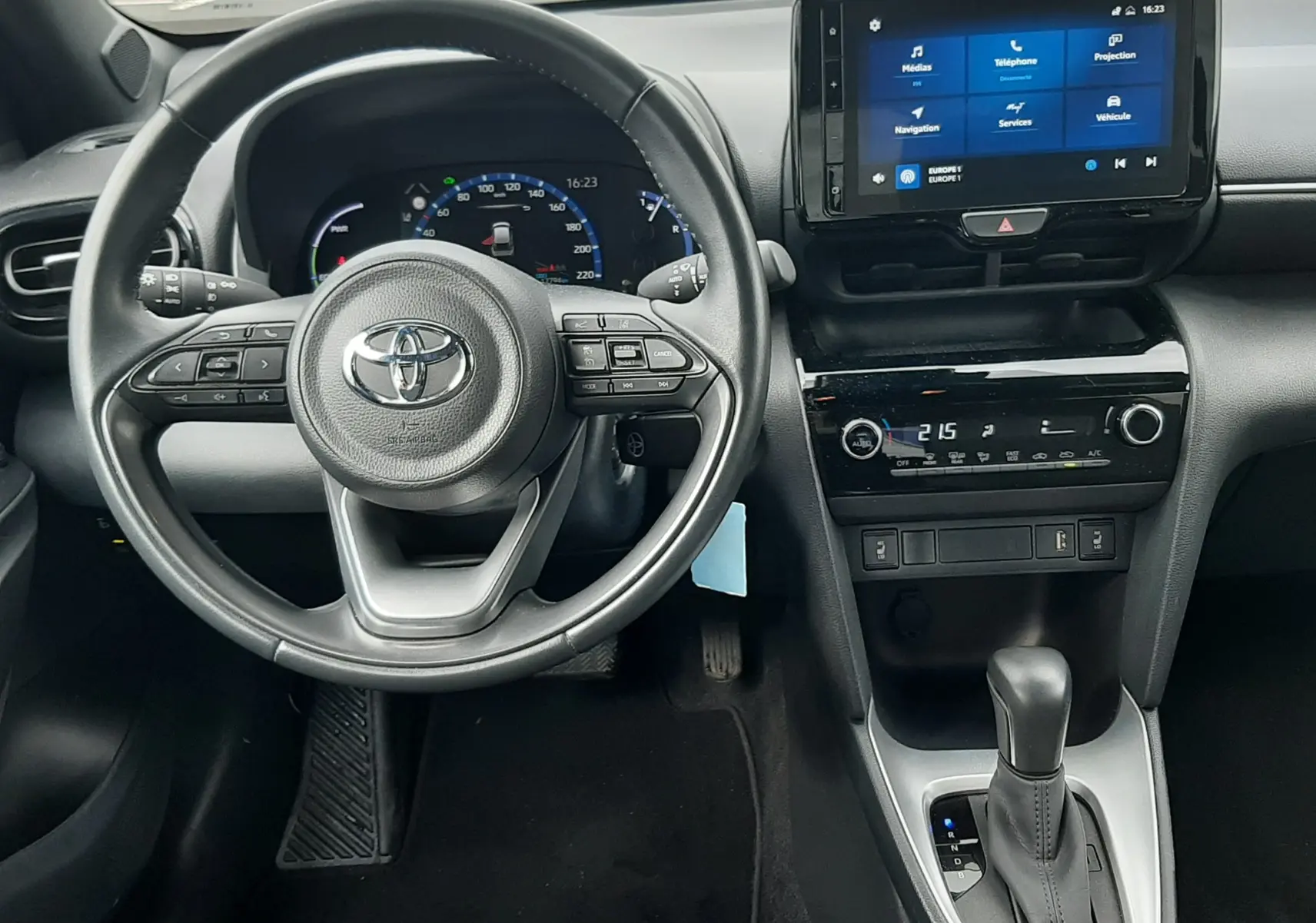 Vue intérieure du poste de conduite de la Toyota Yaris Cross 2024 hybride, avec volant multifonction et écran tactile central allumé.