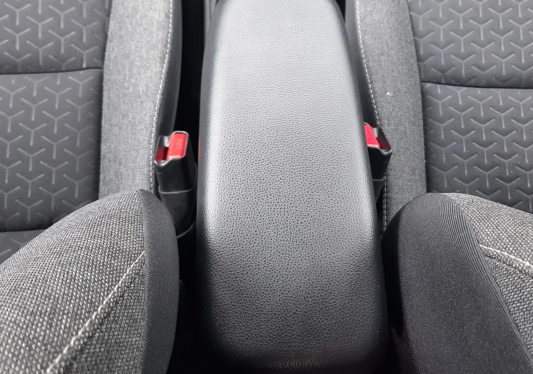 Vue plongeante sur l'accoudoir central noir et les sièges tissu gris de la Toyota Yaris Cross 2024.