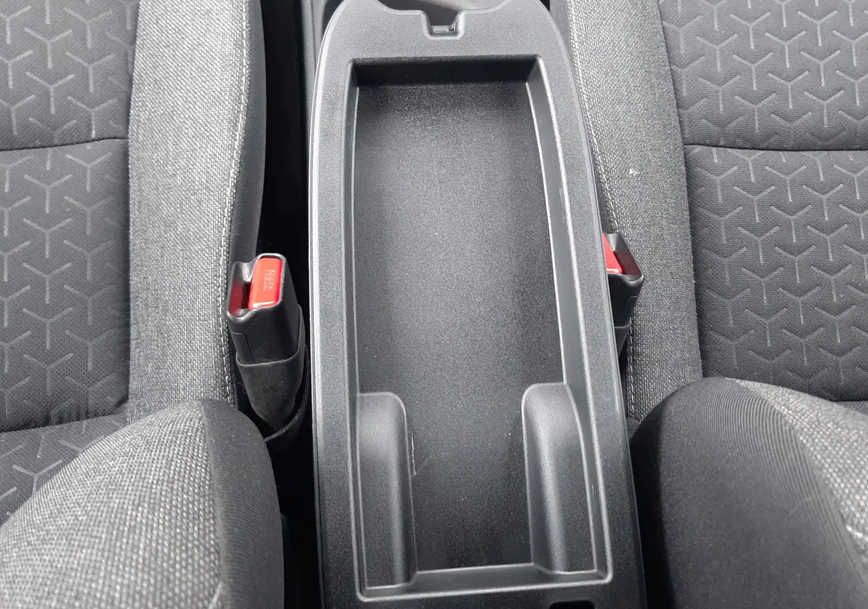 Vue plongeante sur la console centrale noire entre les sièges tissu gris foncé de la Toyota Yaris Cross 2024.