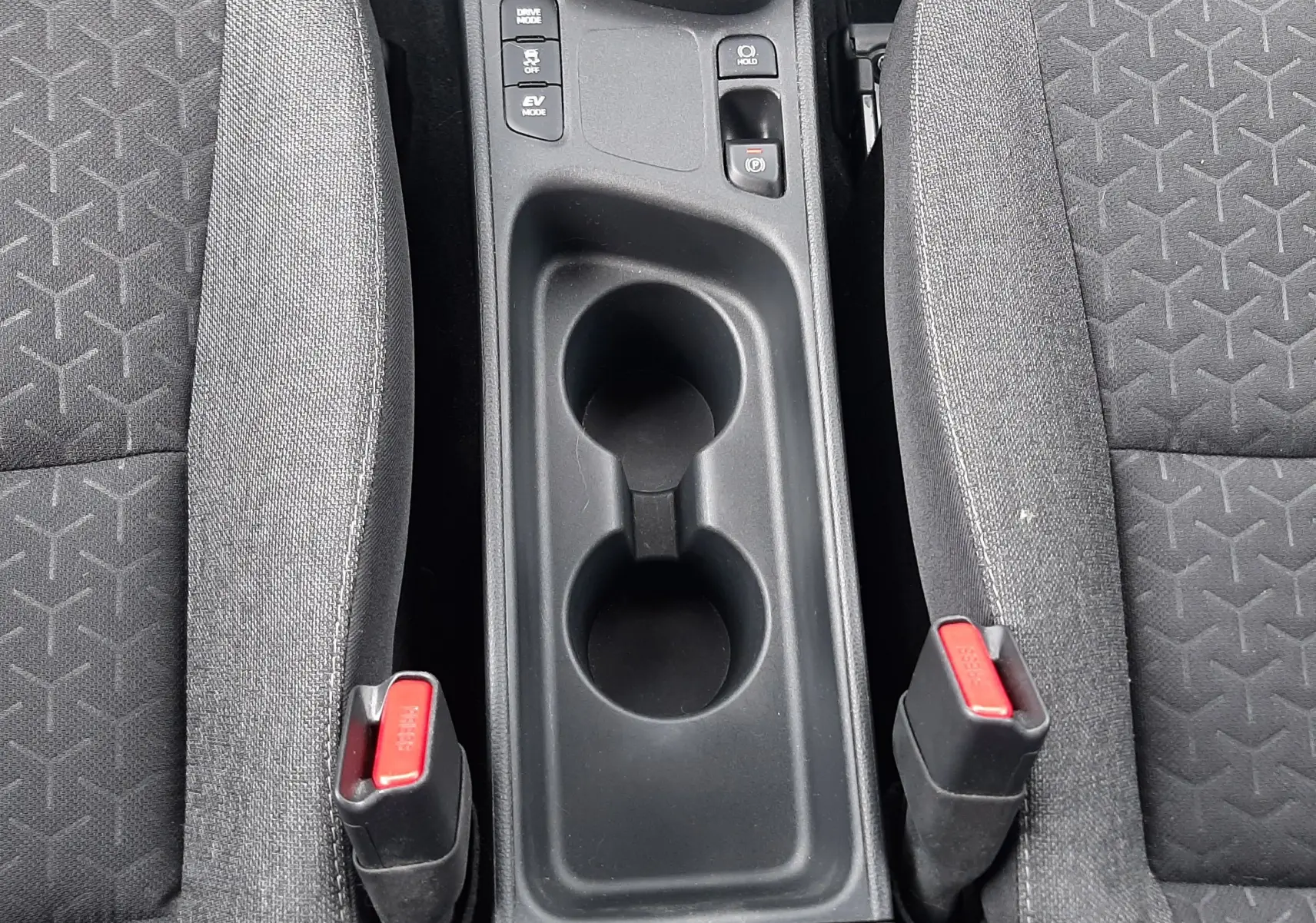 Vue plongeante sur la console centrale noire et les sièges tissu gris foncé du Toyota Yaris Cross 2024 hybride.