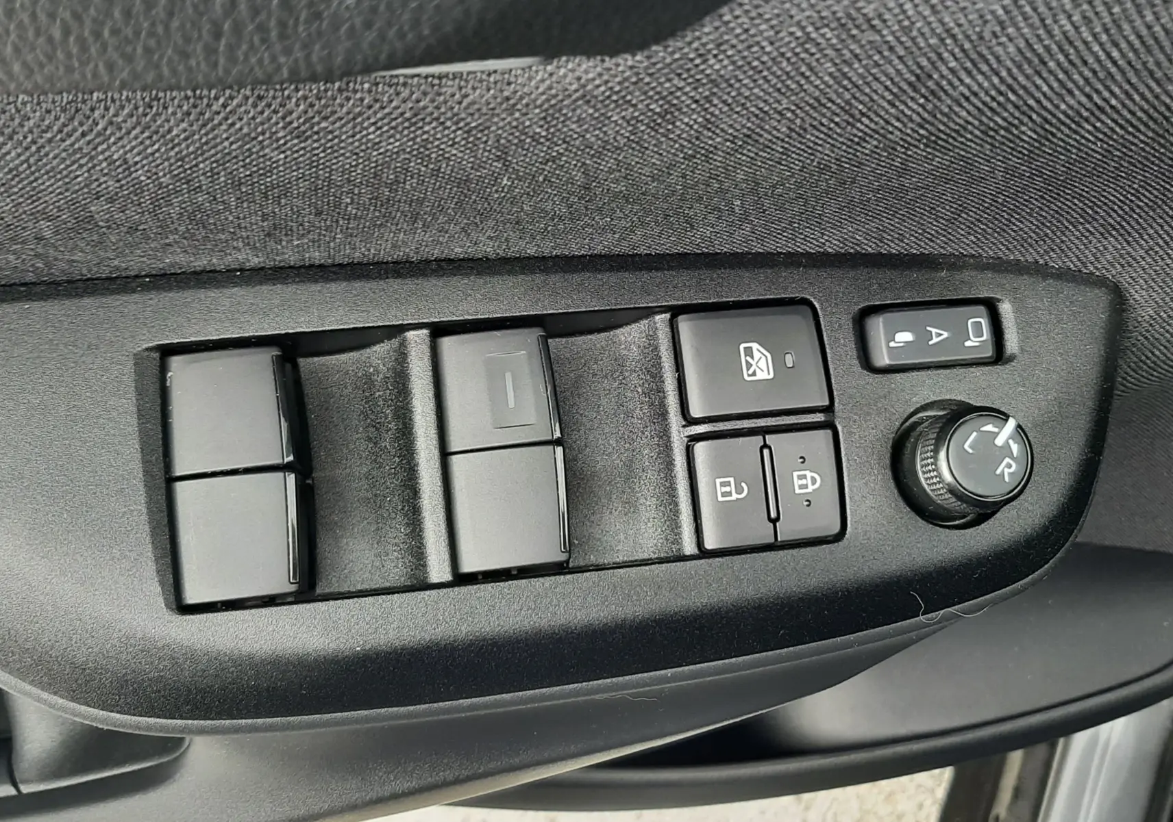 Gros plan sur les commandes de lève-vitres et réglage des rétroviseurs côté conducteur de la Toyota Yaris Cross gris atlas 2024.