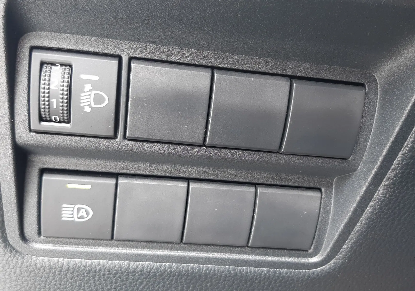 Panneau de commandes intérieures noires avec réglage des phares et bouton d'assistance sur Toyota Yaris Cross 2024.