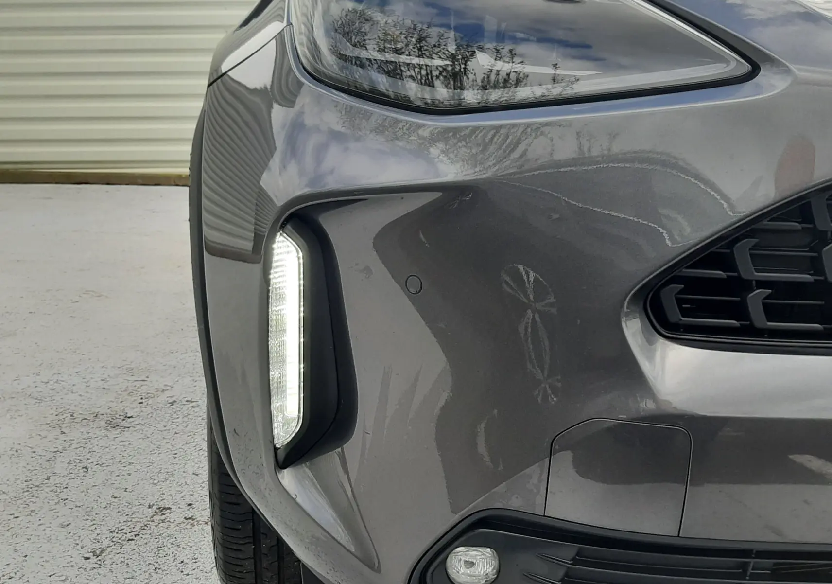 Gros plan sur l'avant droit gris atlas métal du Toyota Yaris Cross 2024, avec phare et feux LED verticaux allumés.