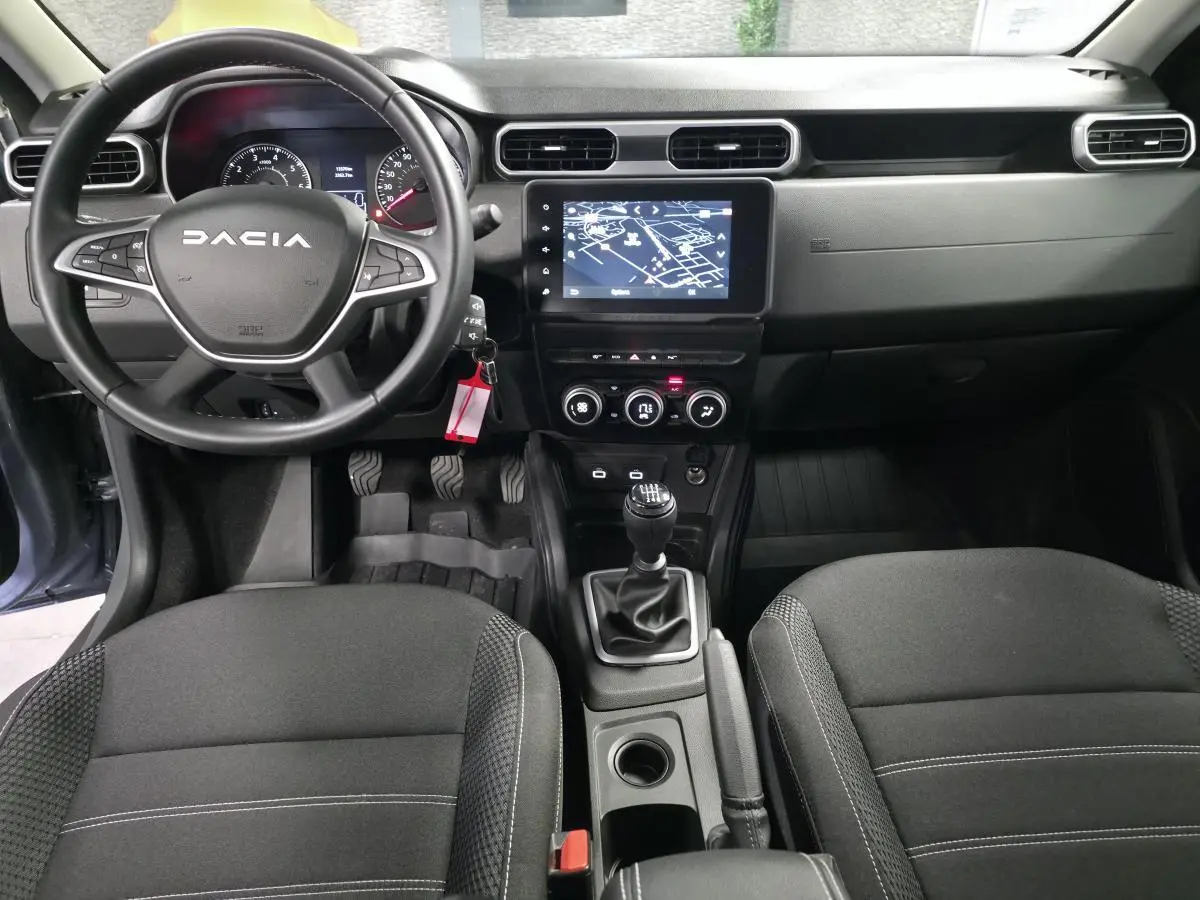 Vue intérieure avant du Dacia Duster 2024, tableau de bord noir avec écran tactile et volant multifonction.