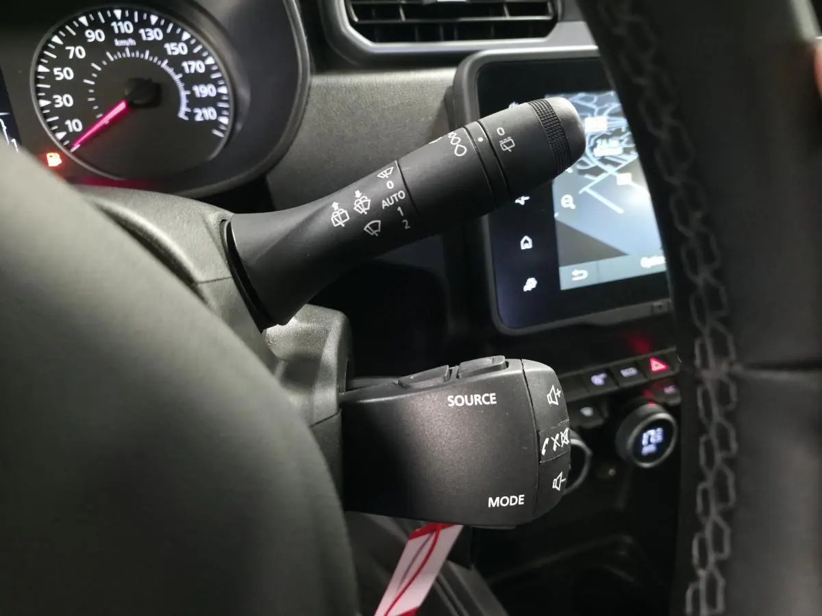 Gros plan sur les commandes au volant noir du Dacia Duster 2024, avec écran tactile et compteur partiel en arrière-plan.