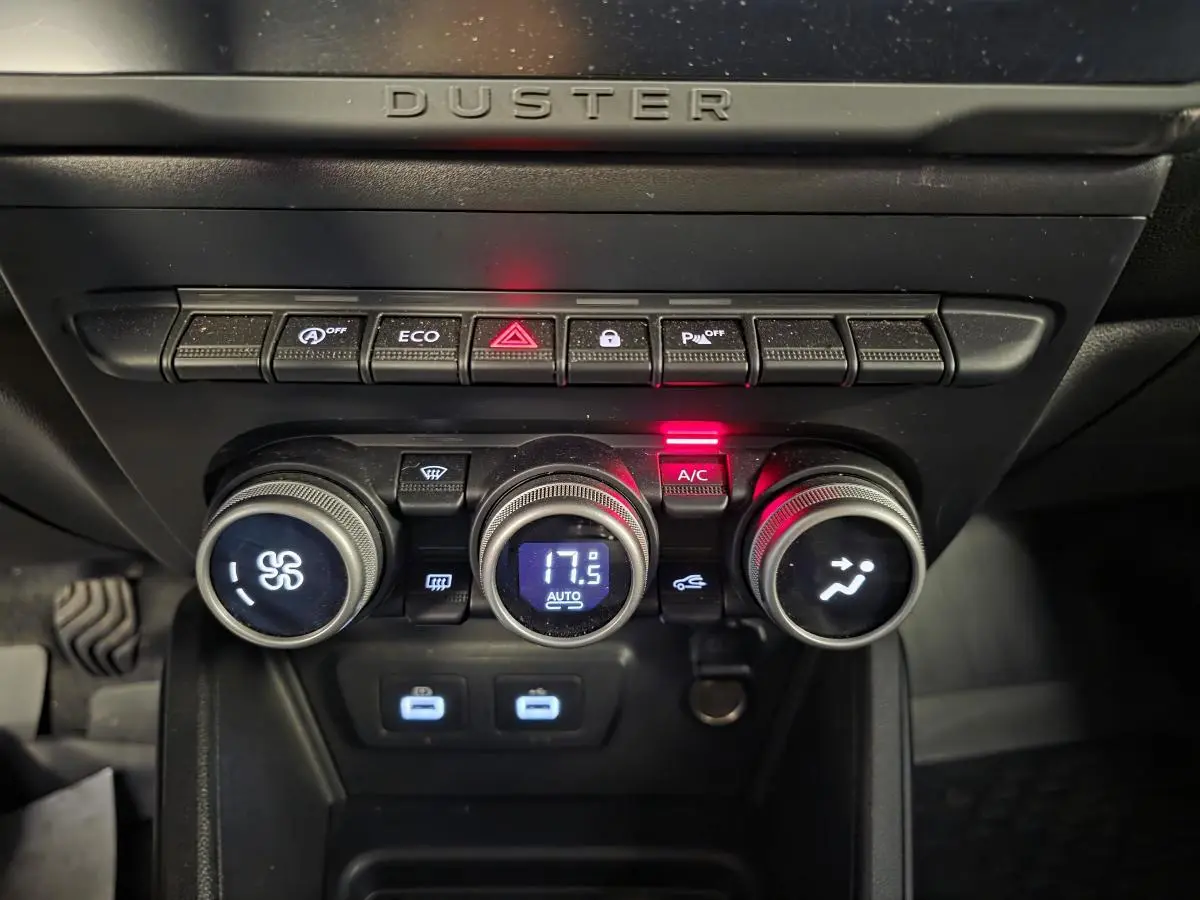 Vue rapprochée de la console centrale du Dacia Duster 2024 avec commandes climatisation automatique et boutons fonctionnels éclairés.