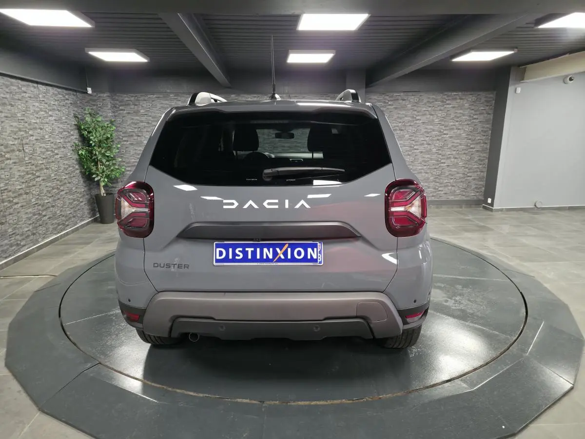 Vue arrière d'un Dacia Duster gris urbain avec logo blanc et feux arrière au design carré, en showroom.