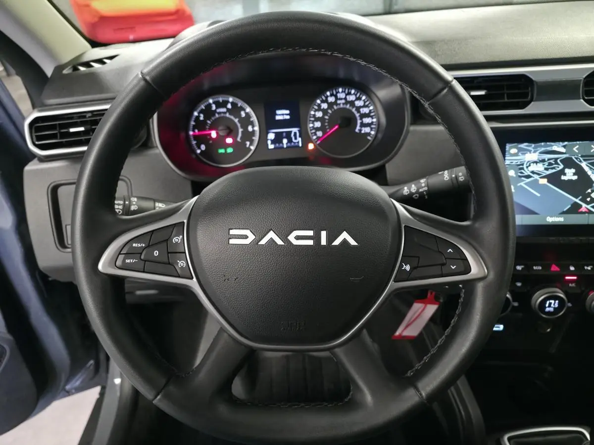 Vue rapprochée du volant noir DACIA avec commandes intégrées et tableau de bord numérique du Duster 2024.