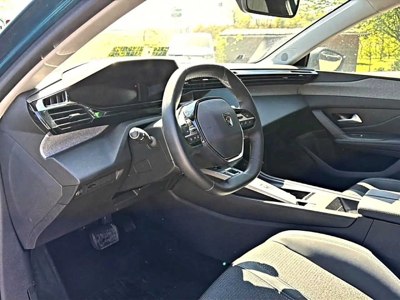 Vue intérieure côté conducteur du Peugeot 408 Hybrid bleu, avec volant cuir et tableau de bord moderne noir.