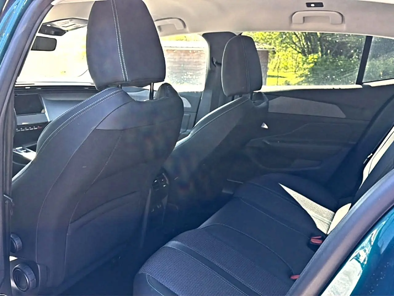 Vue intérieure arrière de la Peugeot 408 Hybrid 145 allure bleu, montrant les sièges arrière et les dossiers avant en tissu noir.