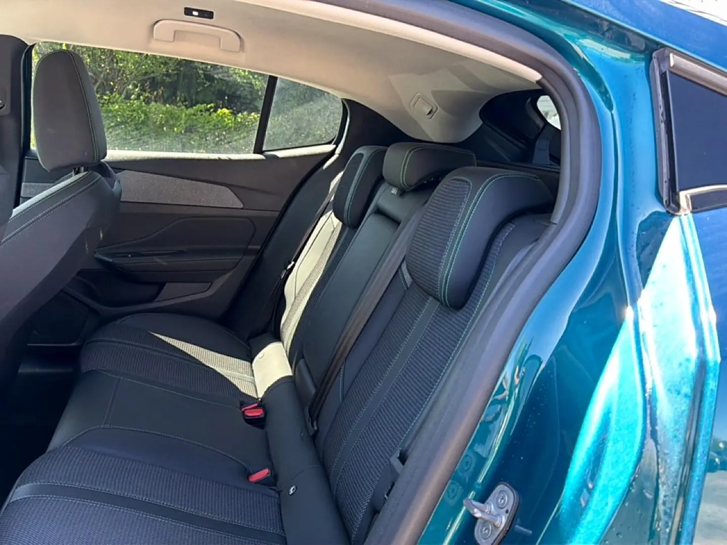 Vue intérieure côté arrière droit d'une Peugeot 408 Hybrid 145 allure e-dcs6 bleu, montrant la banquette arrière en tissu et cuir.