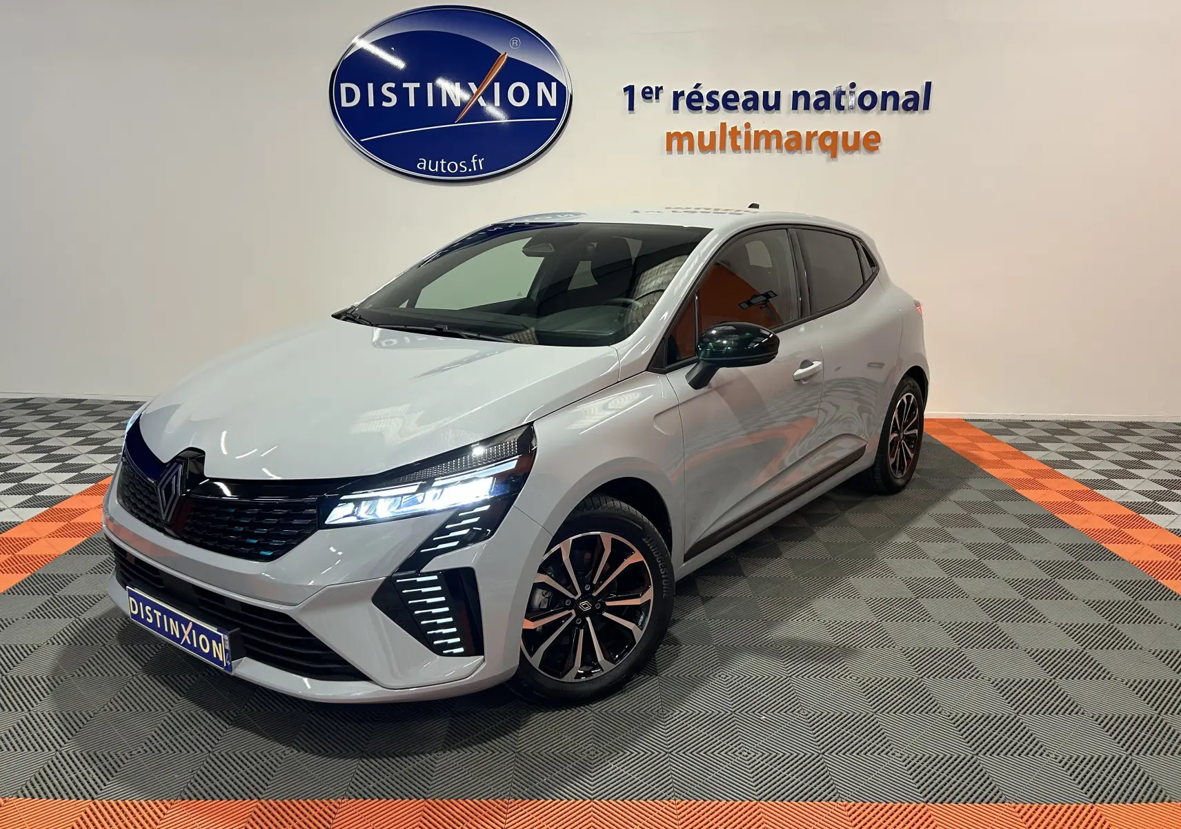 Renault Clio V E-Tech gris Rafale vue 3/4 avant droit avec phares LED allumés en showroom.